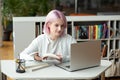 Hipster teen girl student with pink hair watch video online webinar learn on laptop at library Royalty Free Stock Photo