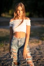 Hipster teenage girl looks at camera while posing on sunset outdoors. Fashion young model walks at beach in sunny Royalty Free Stock Photo