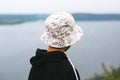 Hipster teenager in bucket hat standing on top of rock mountain and looking on river, view from back. Atmospheric calm moment. Royalty Free Stock Photo