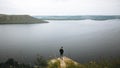 Hipster teenager standing on top of rock mountain and looking on river, view from back. Atmospheric tranquil moment. Young guy Royalty Free Stock Photo