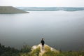 Hipster teenager standing on top of rock mountain and looking on river, view from back. Atmospheric tranquil moment. Young guy Royalty Free Stock Photo