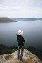 Hipster teenager standing on top of rock mountain and looking on river, view from back. Young stylish guy exploring and traveling Royalty Free Stock Photo