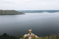 Hipster teenager standing on top of rock mountain and looking on river, view from back. Young stylish guy exploring and traveling Royalty Free Stock Photo