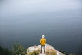 Hipster teenager in yellow pullover standing on top of rock mountain and looking on river, view from back. Young stylish guy Royalty Free Stock Photo