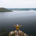 Hipster teenager in yellow pullover standing on top of rock mountain and looking on river, view from back. Young stylish guy Royalty Free Stock Photo