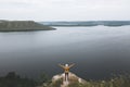 Hipster teenager in yellow pullover standing on top of rock mountain and raising hands up. Young stylish guy exploring and Royalty Free Stock Photo