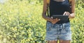 Hipster texting message on tablet or technology, mock up of blank screen. Girl using computer on yellow flowers background close Royalty Free Stock Photo