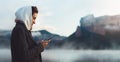 Hipster tourist using smartphone planning trip on foggy lake, mist in mountain nature, traveler girl hold mobile phone, enjoy wifi