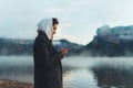 Hipster tourist using smartphone trip on foggy lake, mist in mountain nature, traveler girl hold mobile phone, enjoy wifi internet