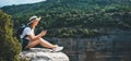 Hipster traveler in hat and backpack ralaxing in nature and using internet on smartphone, tourist girl chatting on cellphone Royalty Free Stock Photo