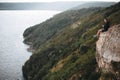 Hipster traveler sitting on top of rock mountain and enjoying amazing view on river. Young guy exploring and traveling. Royalty Free Stock Photo