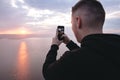 Hipster traveler taking photo on phone of amazing sunset view on river while standing on top of rock mountain. Atmospheric  moment Royalty Free Stock Photo