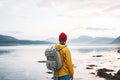 Hipster traveler wearing backpack and yellow raincoat looking away at mountain and fjord