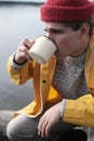 Hipster traveler in yellow raincoat holding metal mug. 