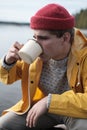 Hipster traveler in yellow raincoat holding metal mug. 