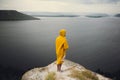 Hipster traveler in yellow raincoat standing on cliff and looking at lake in windy moody day. Wanderlust and travel concept. Man Royalty Free Stock Photo