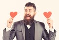 Hipster wears formal suit. Happy man with long beard and smiling face. Bearded man smiles and holds red hearts. Dating