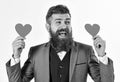 Hipster wears formal suit. Happy man with long beard and smiling face. Bearded man smiles and holds red hearts. Dating