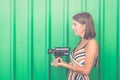 Young fashionable girl with vintage camcorder against green wall outdoors. Royalty Free Stock Photo