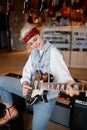 Hipster woman playing guitar connected to amplifier over shop store background