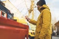 Hipster with yellow backpack, jacket, cap, coffee of thermo cup holding in the hands smartphone, freelance using gadget mobile Royalty Free Stock Photo