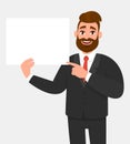 Hipster young businessman showing blank white poster and pointing finger. Happy trendy person holding empty banner. Royalty Free Stock Photo