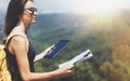 Hipster young girl with backpack enjoying panoramic mountain sea, map and looking at horizon. Tourist traveler texting on tablet