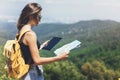 Hipster young girl with backpack enjoying panoramic mountain sea, using map and looking at horizon. Tourist traveler texting