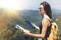 Hipster young girl with backpack enjoying panoramic mountain sun sea, using map and looking at horizon. Tourist traveler texting