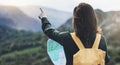 Hipster young girl with bright backpack enjoying sunset on peak of foggy mountain, looking a map and poining hand. Tourist travele Royalty Free Stock Photo