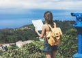 Hipster young girl with bright backpack looking at a map and poining hand the travel plan. View from the back of the tourist Royalty Free Stock Photo