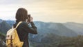 Hipster young girl with bright backpack taking photo of amazing landscape sunset on vintage camera on peak of foggy mountain Royalty Free Stock Photo