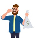 Hipster young man looking through magnifying glass or magnifier and holding cash, money bag with dollar sign. Bearded person.