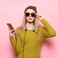 Hipster young woman using cell phone and selecting music to listen on headphones.