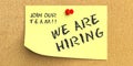 We Are Hiring, Join Our Team phrase in yellow post it on bulletin board cork background