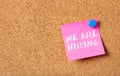 We Are Hiring phrase in pink post it, space on bulletin board cork background. Staff wanted concept