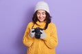 Hirizontal shot of beautiful young girl wearing cap, knitted sweater holding camera and looking at digital photos, spending winter Royalty Free Stock Photo