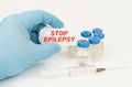In his hand is a piece of paper with the inscription - STOP EPILEPSY, next to it lies a syringe and injection jars.