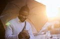 His phone is flooded with notifications of good news. a young businessman using a cellphone while holding an umbrella on