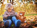 His teddy is always by his side. an adorable little boy using his tablet while sitting outdoors during autumn. Royalty Free Stock Photo
