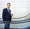 On his way to a meeting. Handsome mature businessman using his smartphone on an escalator. Royalty Free Stock Photo