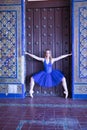 Hispanic adult female classical ballet dancer in blue tutu making figures on the frame of a large wooden door surrounded by