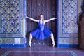 Hispanic adult female classical ballet dancer in blue tutu making figures on the frame of a large wooden door surrounded by