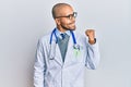 Hispanic adult man wearing doctor uniform and stethoscope smiling with happy face looking and pointing to the side with thumb up Royalty Free Stock Photo