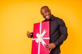 Hispanic american man in black t-shirt getting big gift box in studio yellow background Royalty Free Stock Photo