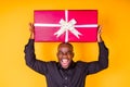 hispanic american man in black t-shirt getting big gift box in studio yellow background Royalty Free Stock Photo