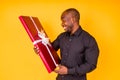 hispanic american man in black t-shirt getting big gift box in studio yellow background Royalty Free Stock Photo