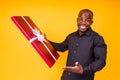 Hispanic american man in black t-shirt getting big gift box in studio yellow background Royalty Free Stock Photo