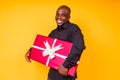 Hispanic american man in black t-shirt getting big gift box in studio yellow background Royalty Free Stock Photo