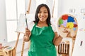 Hispanic brunette woman smiling happy holding painter palette at art studio Royalty Free Stock Photo